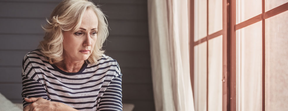 A Woman frowning, sitting on a couch next to a bright window