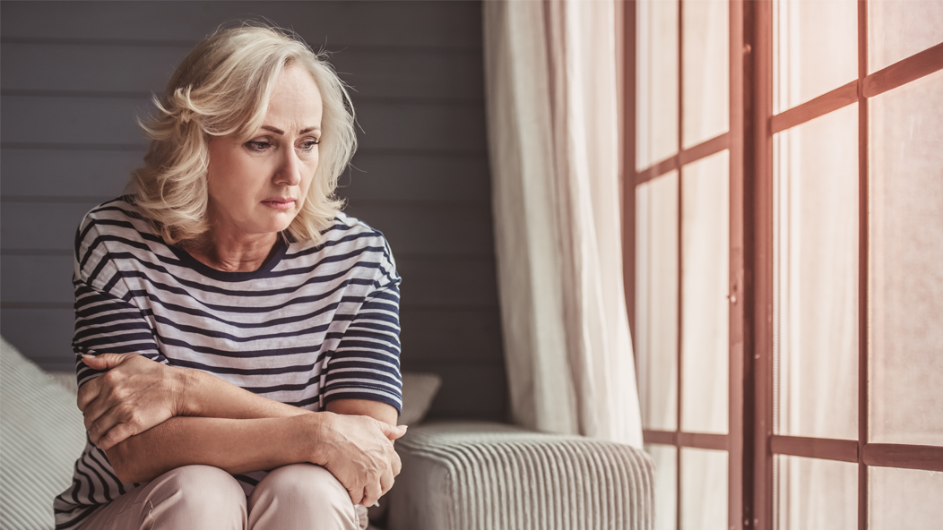 Worried woman sitting on a couch next to a window