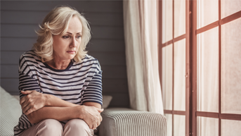 Worried woman sitting on a couch next to a window