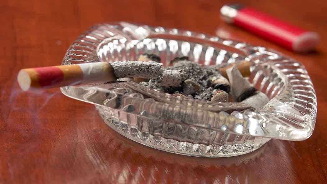 A cigarette perched on the edge of a glass ashtray.