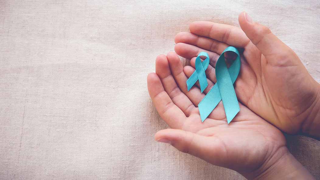 Close-up of a person holding two teal cervical cancer ribbons, one smaller than the other, in cupped hands.