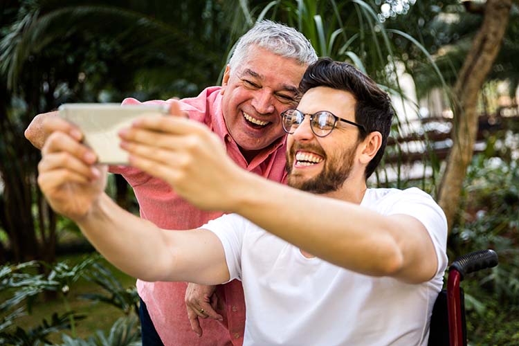 A father and son pose smiling while the son takes a selfie photo of them with his mobile phone.