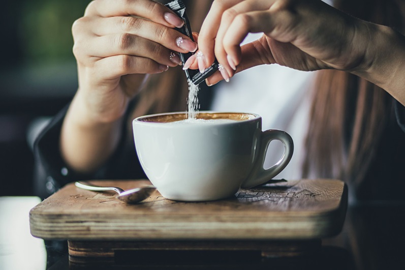 Person pouring sugar into coffee
