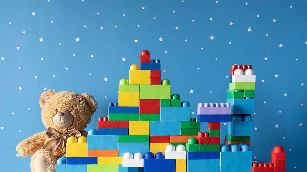 A teddy bear and structures made of LEGO-style building blocks in front of a wall painted blue with star-like accents.