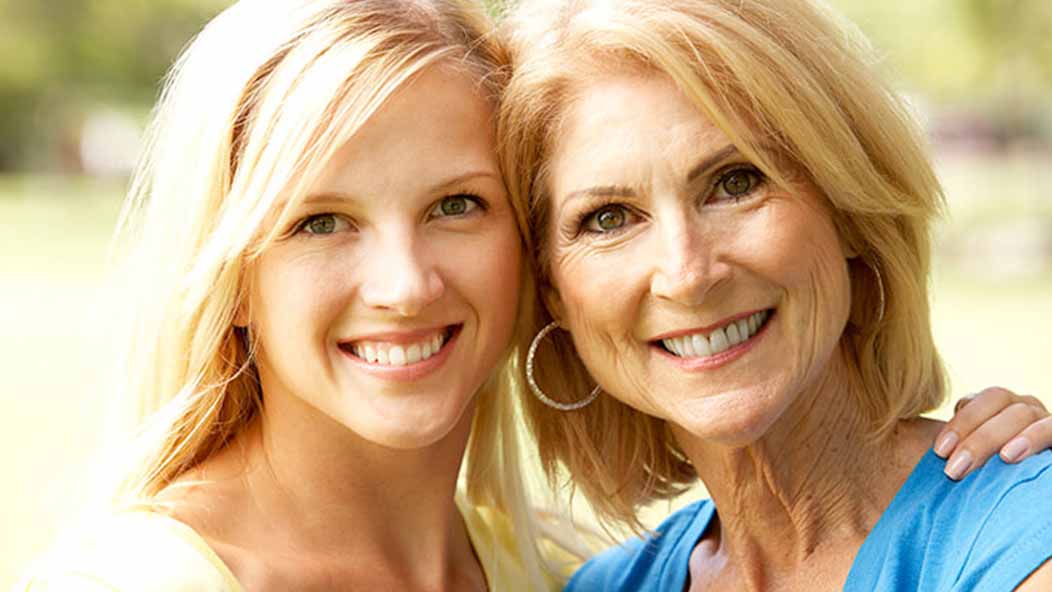 Close-up of a woman and her mother posing with their heads leaned on one another while smiling.