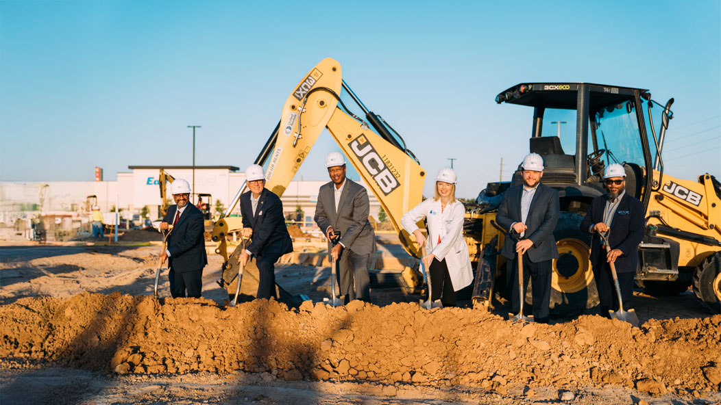 Six people shoveling ground in front of some machinery